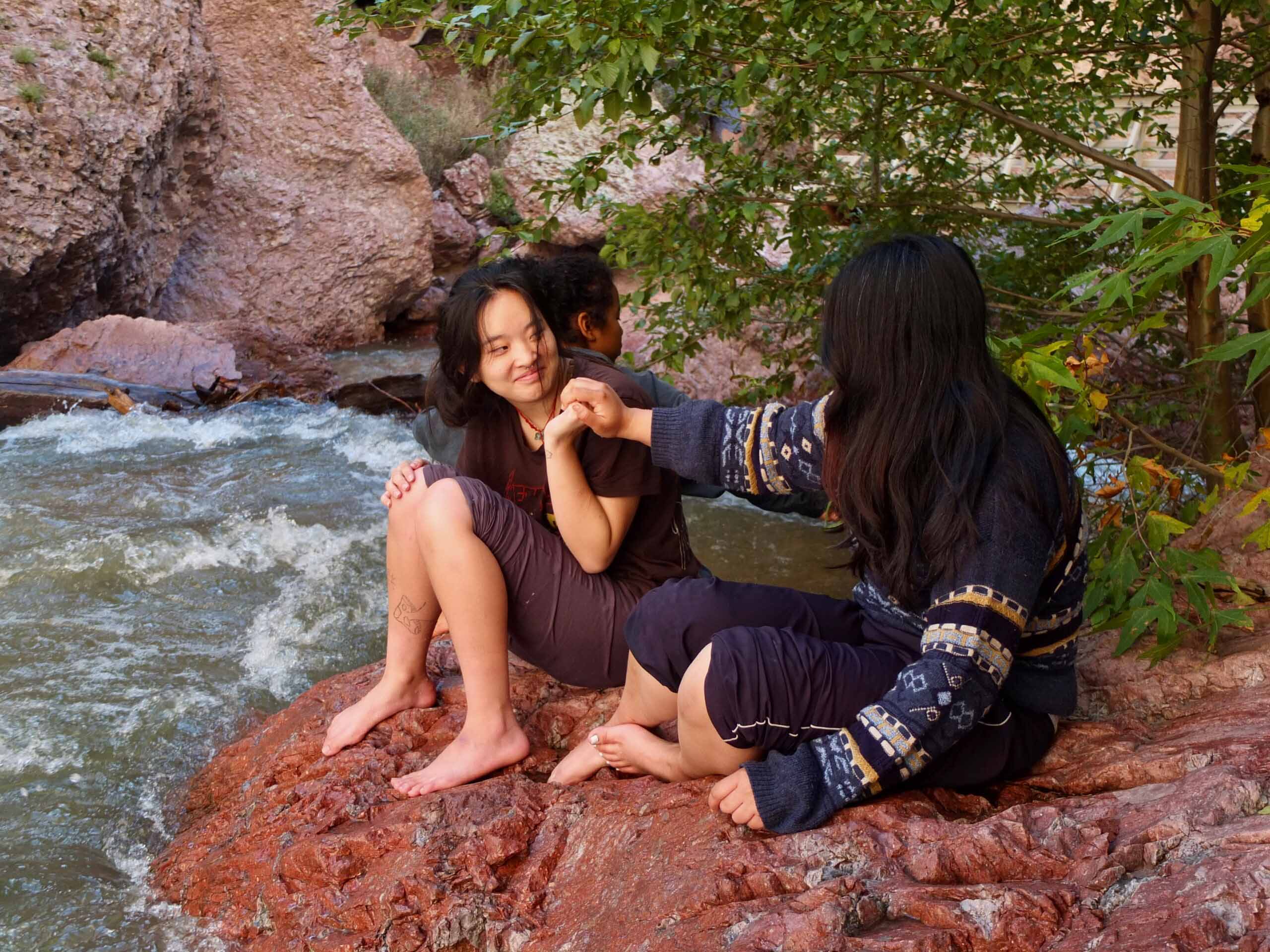 Two students sitting and connecting by the river while holding hands.