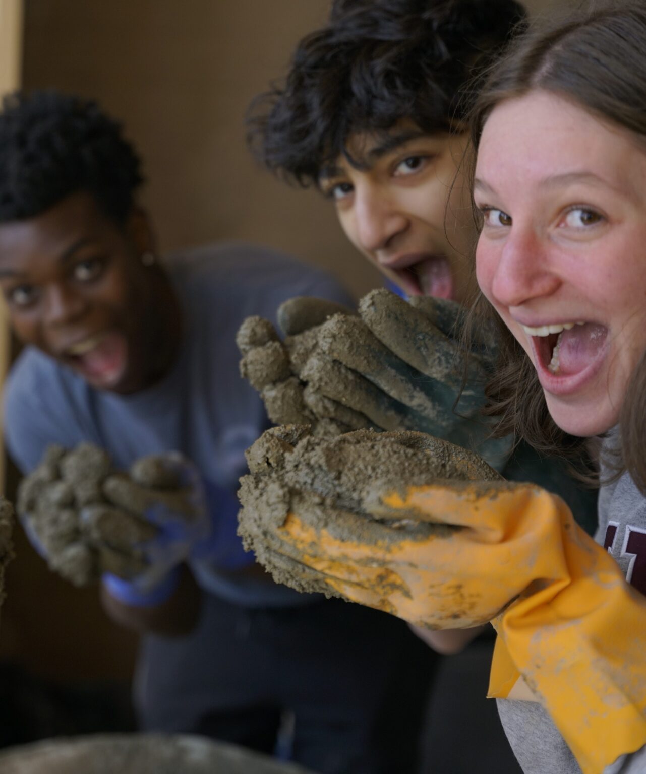 Students from diverse backgrounds partake in sustainability activity with their gloves covered in dirt.