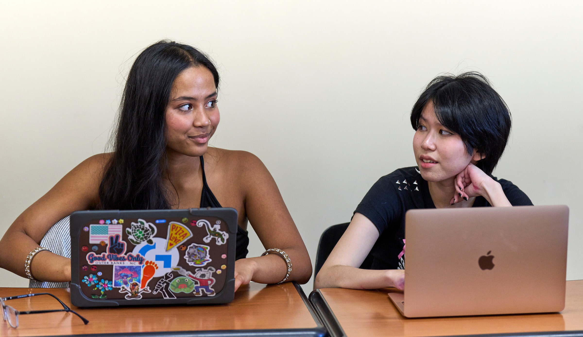 Two students in classroom on their laptops looking at each other.