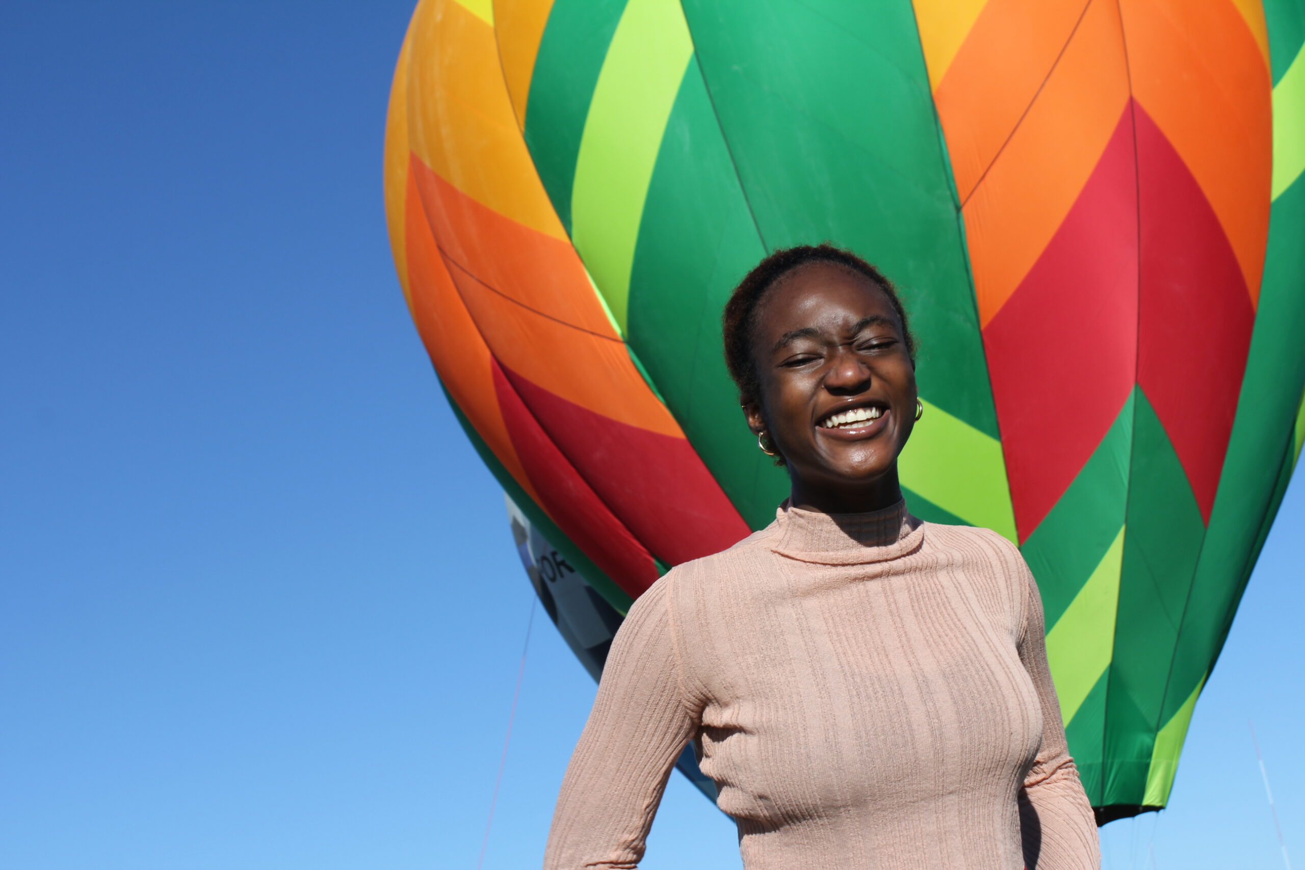 A student smiles before a vibrant hot air balloon at the Albuquerque Balloon Fiesta, embracing global community and adventure at UWC-USA.