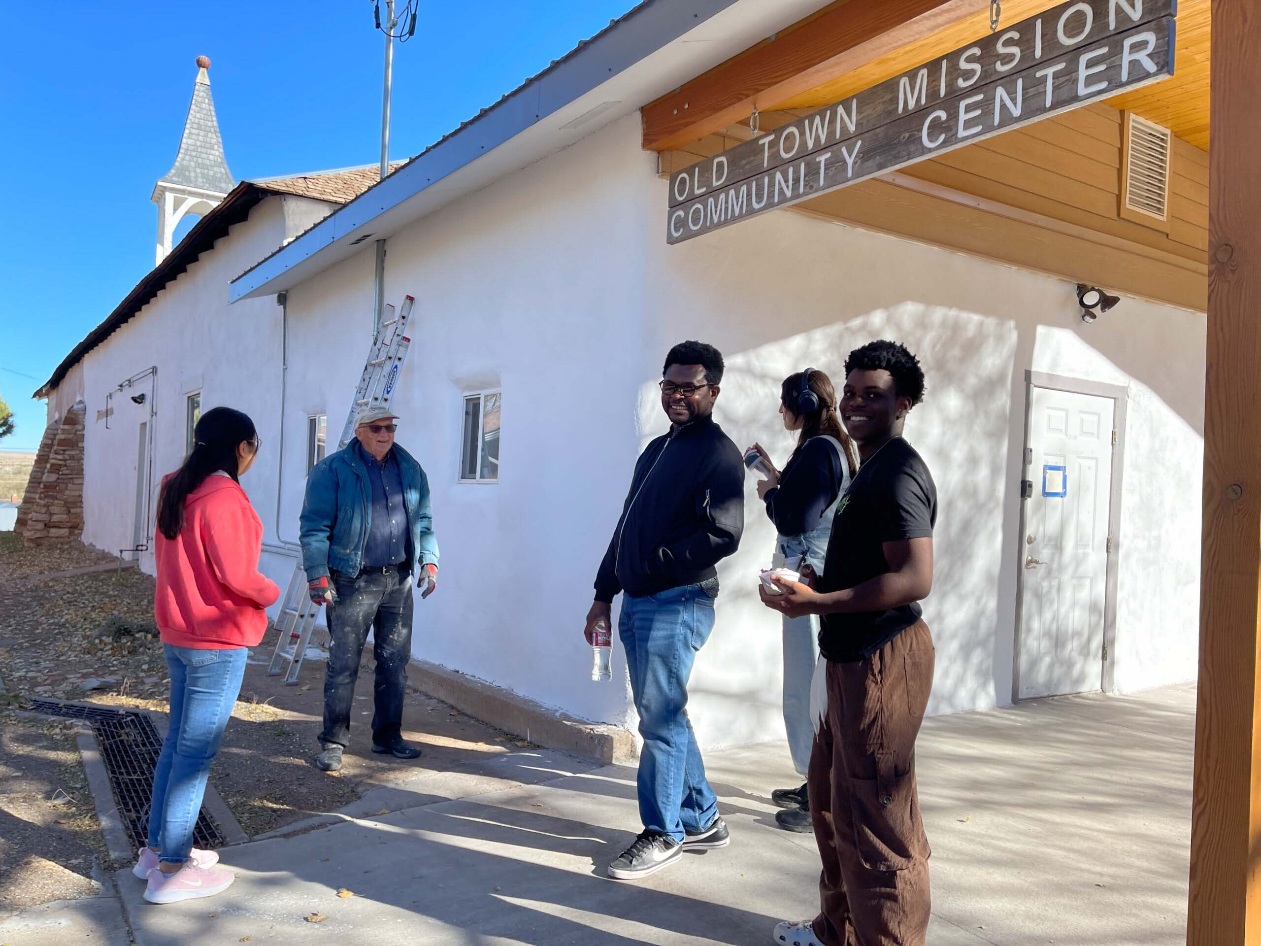 Students representing diverse backgrounds gather outside a community center, collaborating on community service projects in the sunshine.