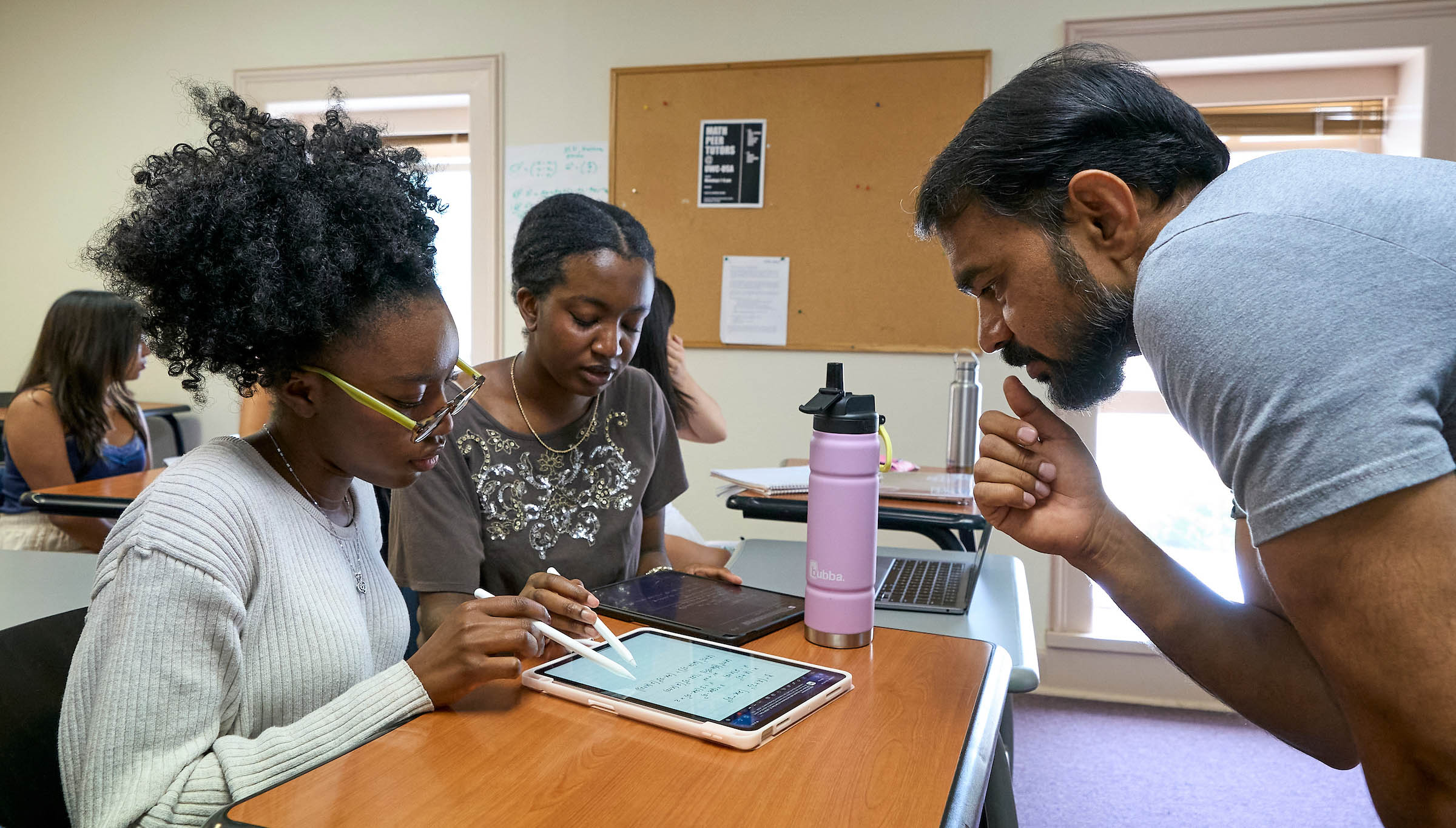 A diverse group collaborates with a teacher on a tablet, engaging in IB academics and fostering global community in the classroom.