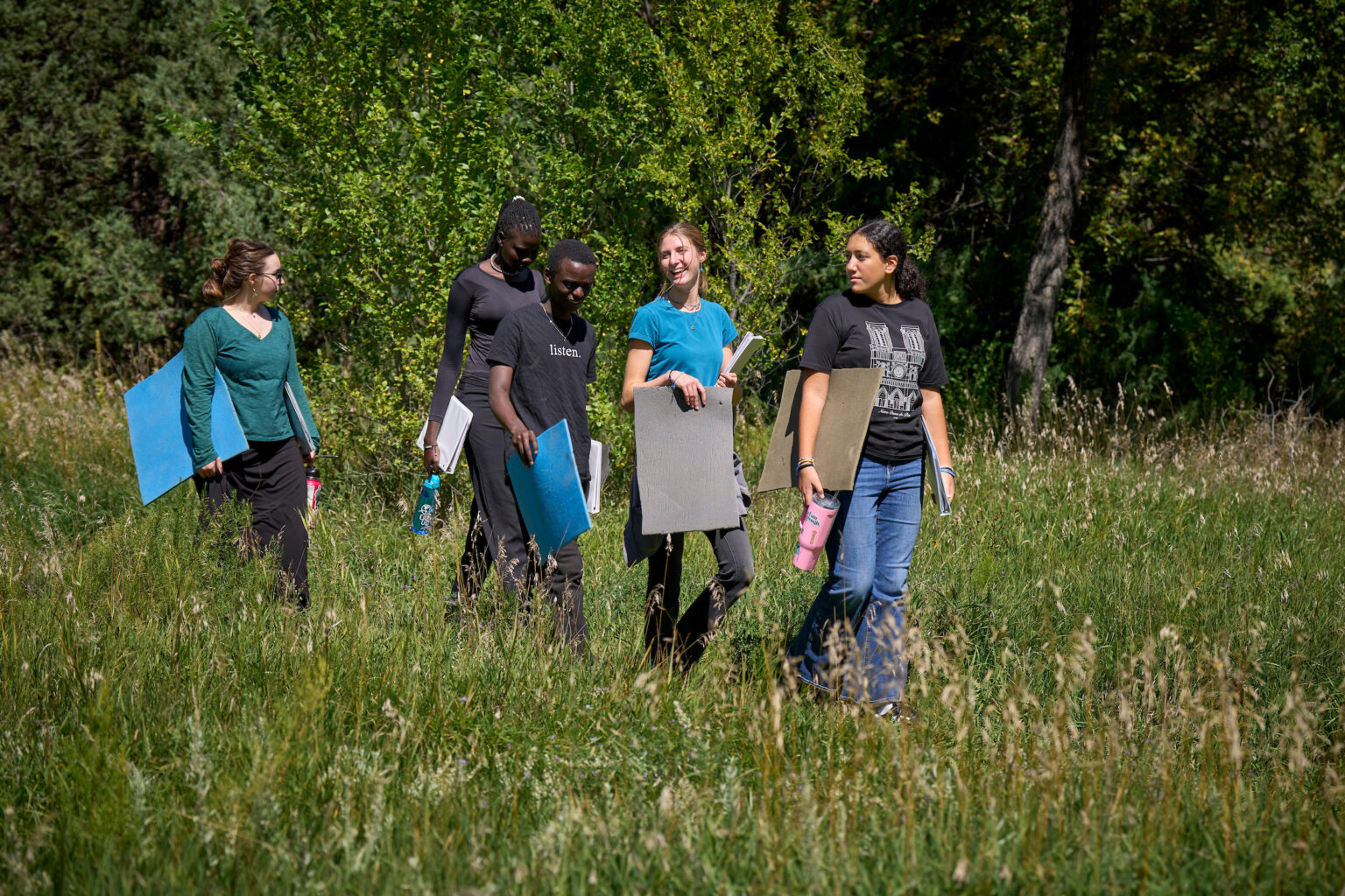 Students from diverse backgrounds walk through a sunlit field with sketchbooks, engaging in outdoor IB learning at UWC-USA.