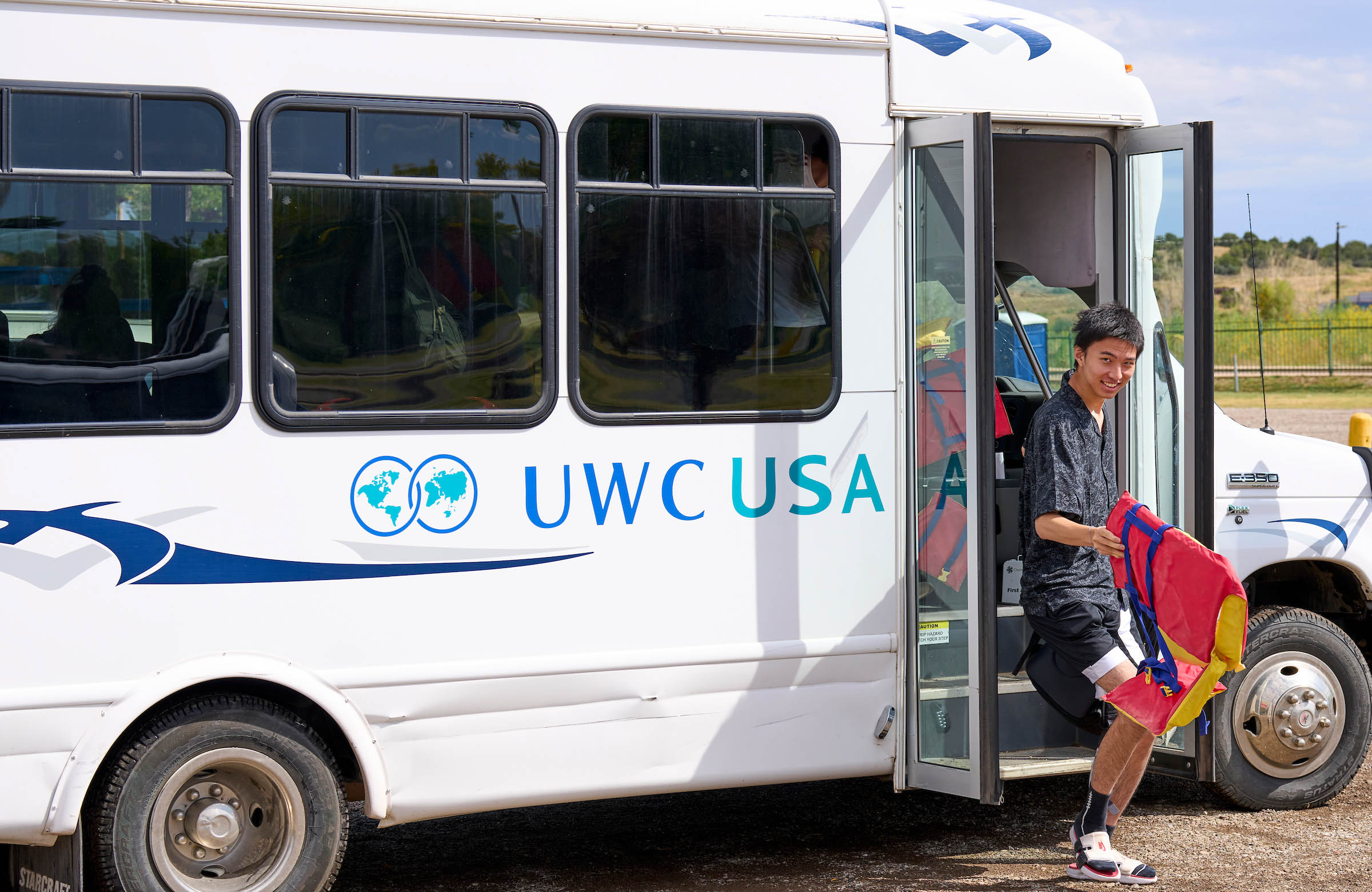 A student smiling and carrying colorful clothing, ready to join the school’s diverse, globally minded community.
