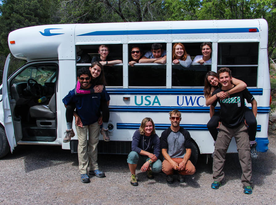 Diverse UWC-USA students gather by a campus bus, reflecting global community, engagement, and joy amid New Mexico’s wilderness.
