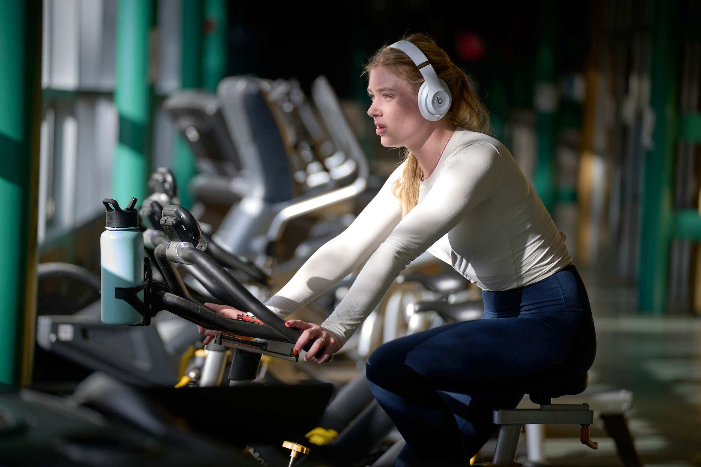 A student from UWC-USA bikes indoors, embracing wellness and focus as sunlight fills the diverse, community-centered campus gym in the Edith Lansing Field House.