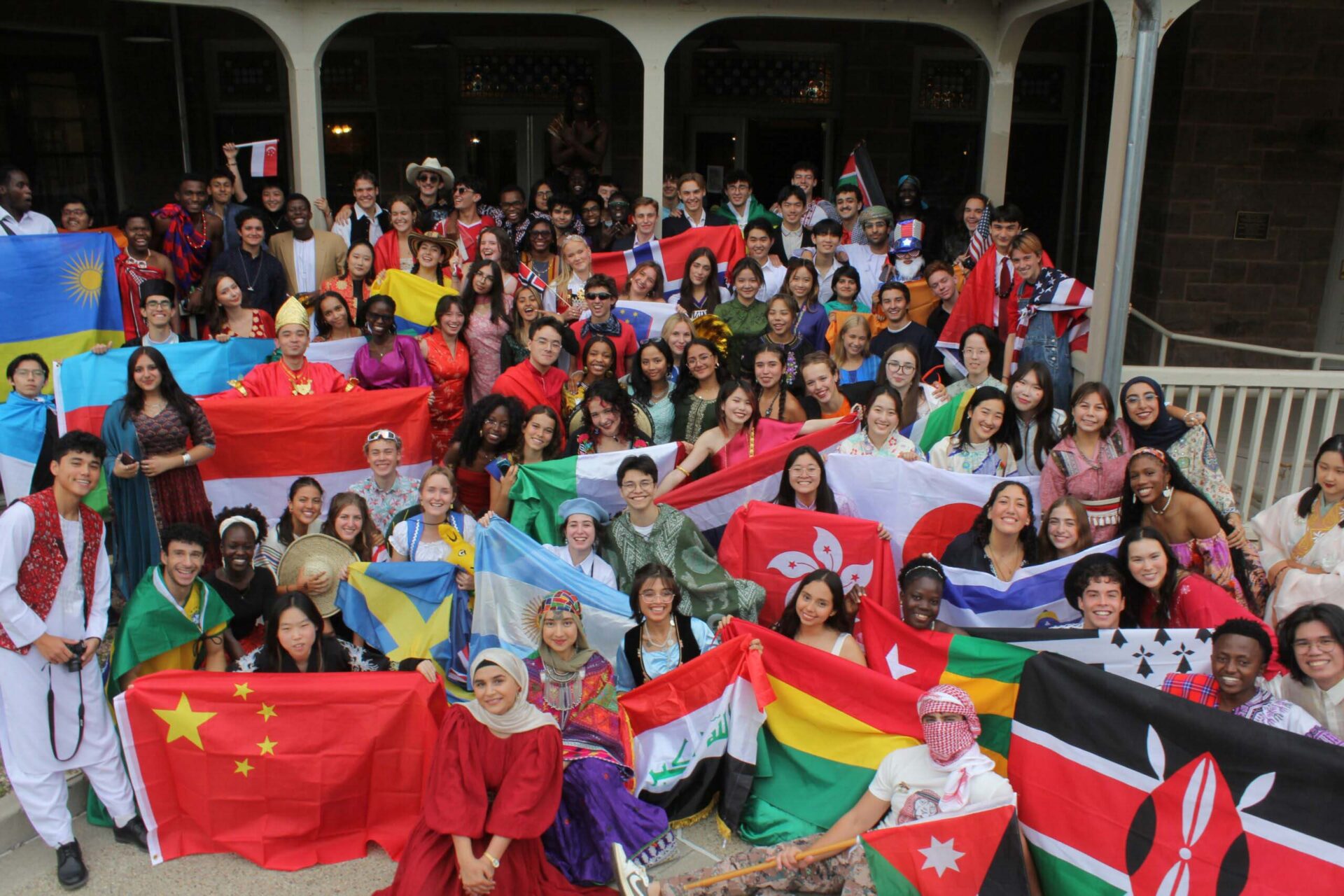 Students in global attire gather outside with international flags, reflecting UWC-USA’s diverse, inclusive community and values.