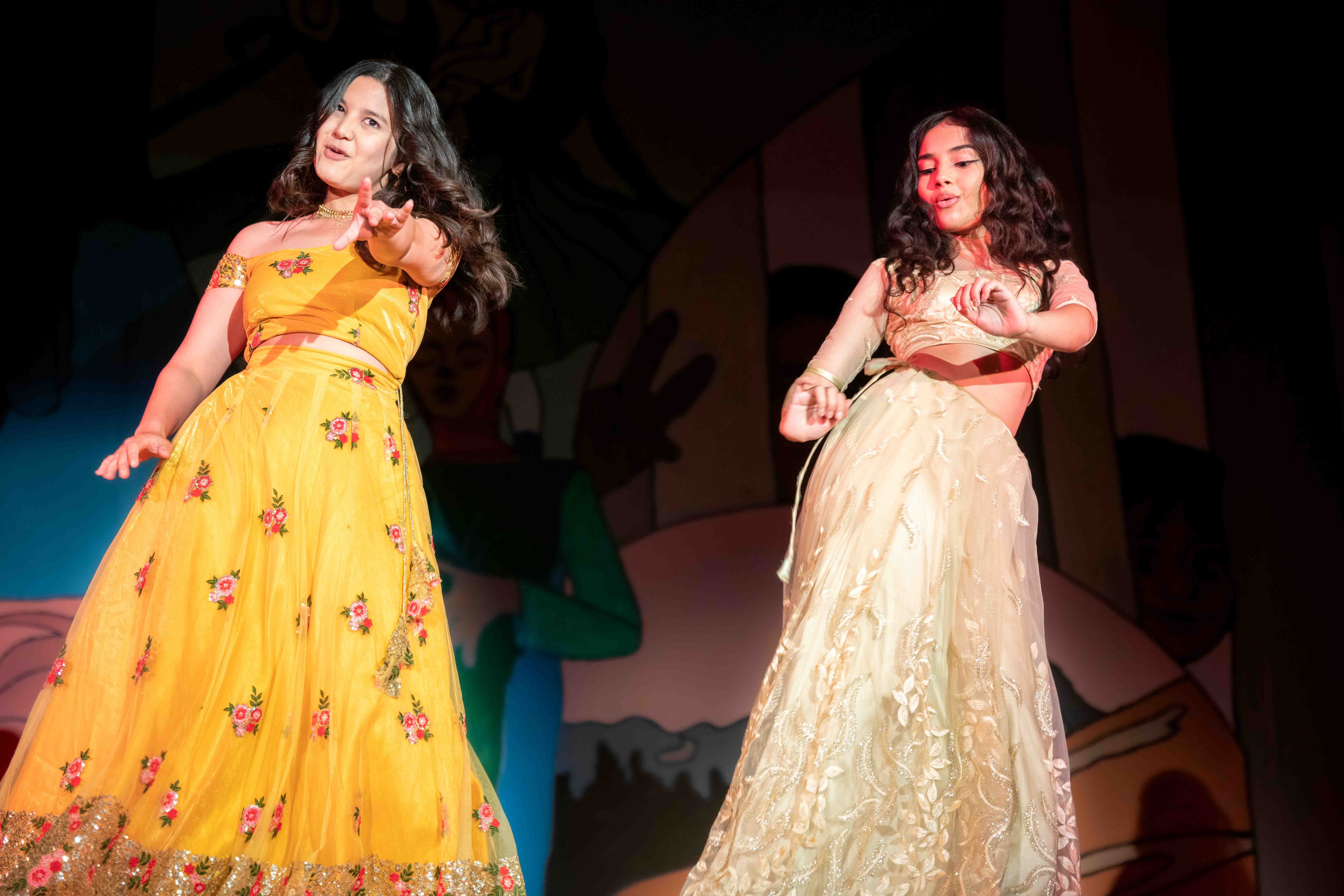 Two students in cultural dresses perform on stage for an arts & culture program show.
