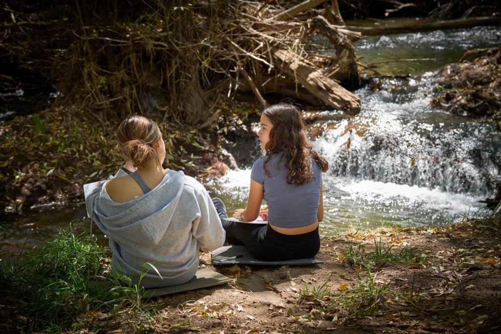 Students from diverse backgrounds connect beside a creek, reflecting UWC-USA’s focus on global learning and nature stewardship.