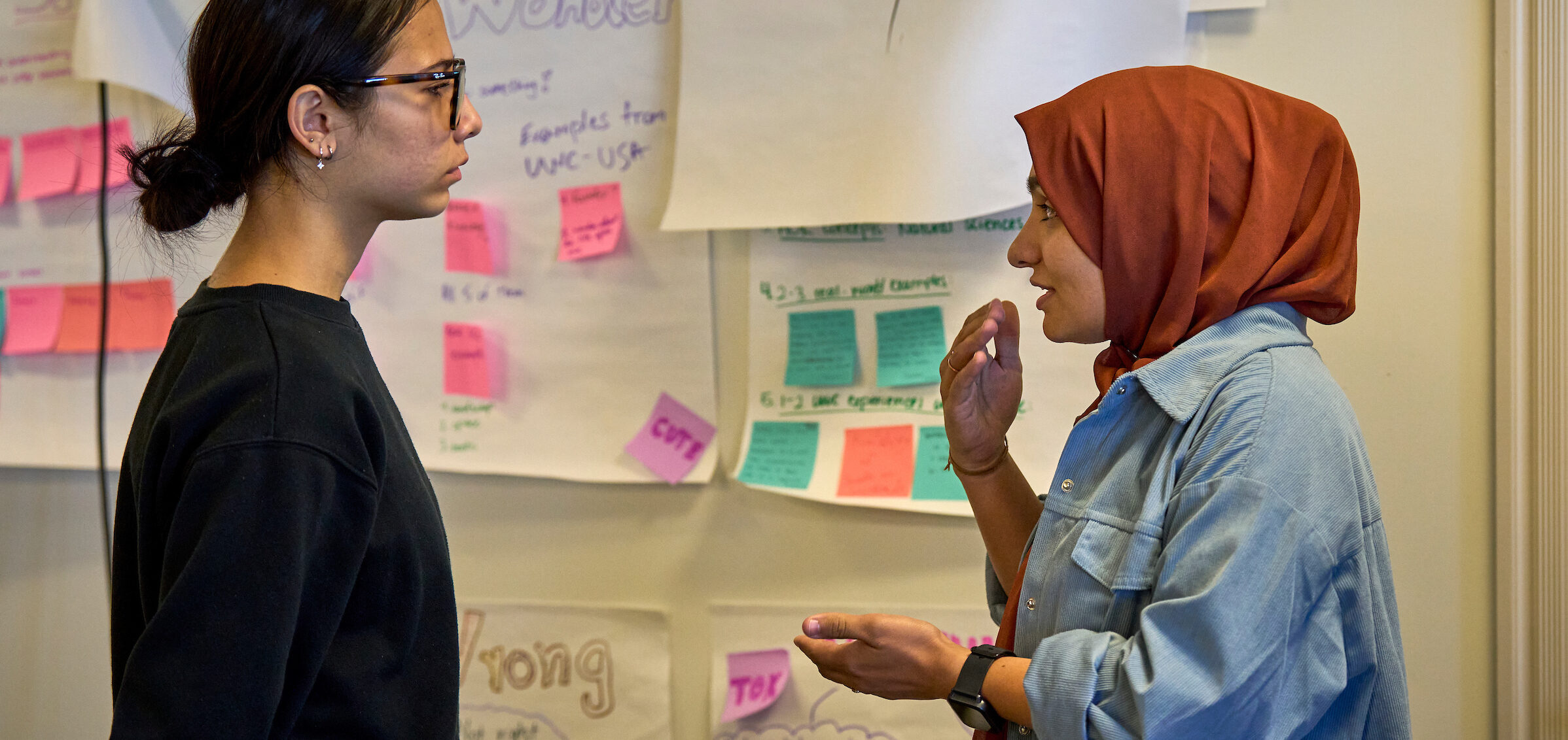 Diverse students collaborate in a workshop, discussing ideas with notes and colorful sticky notes highlighting IB academics and global values.