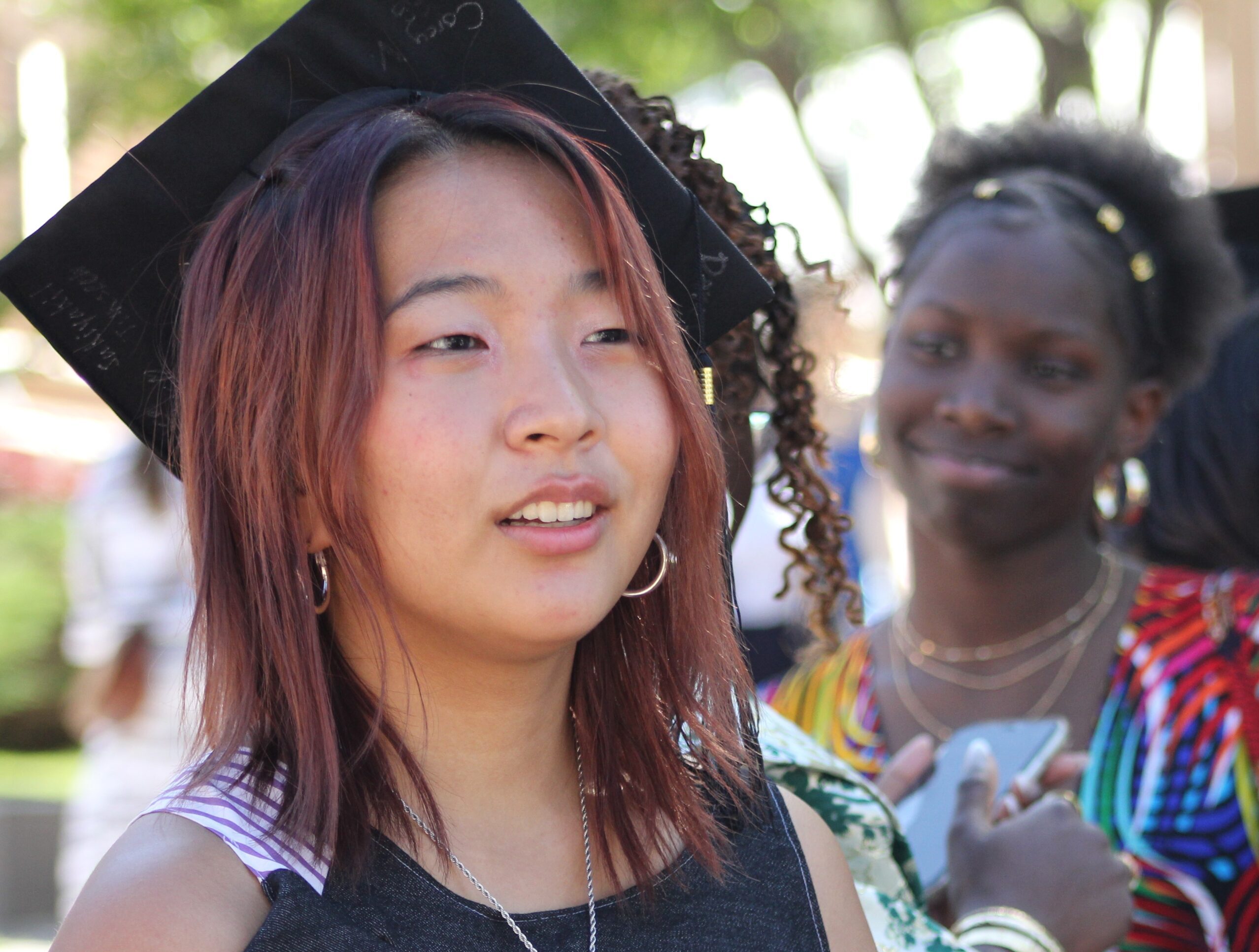 Student in graduation cap looks forward to the future as another student in the background reflects on her future.