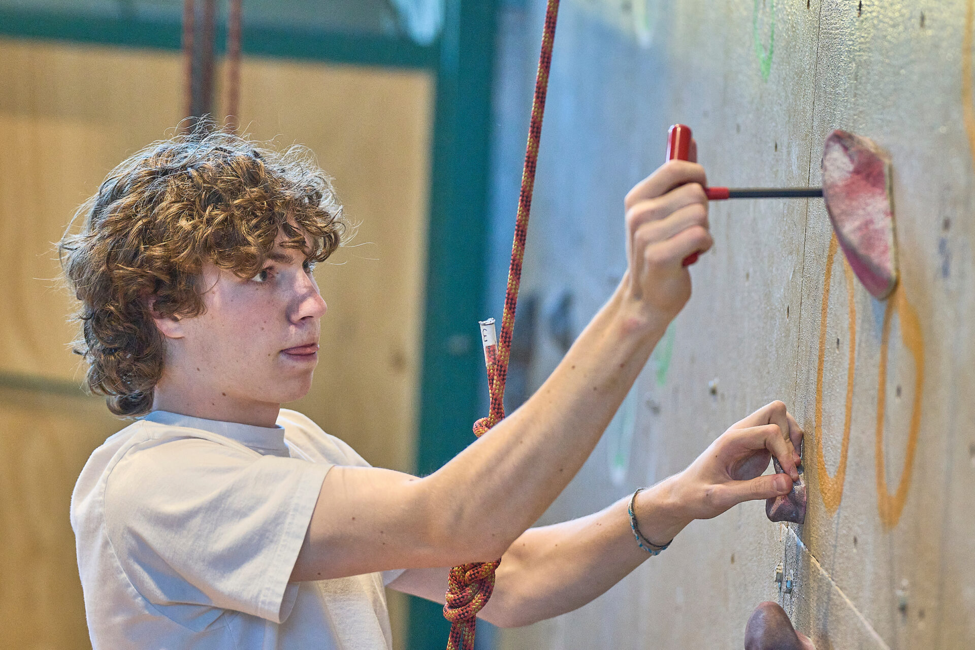 A student with curly hair adjusts a climbing hold during an indoor activity, reflecting UWC-USA’s focus on teamwork and skill-building.