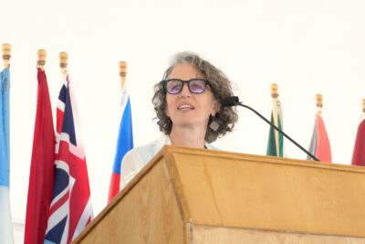 Commencement speaker Pilar Weis '94addresses the UWC-USA community, international flags symbolizing global diversity and unity in Montezuma.