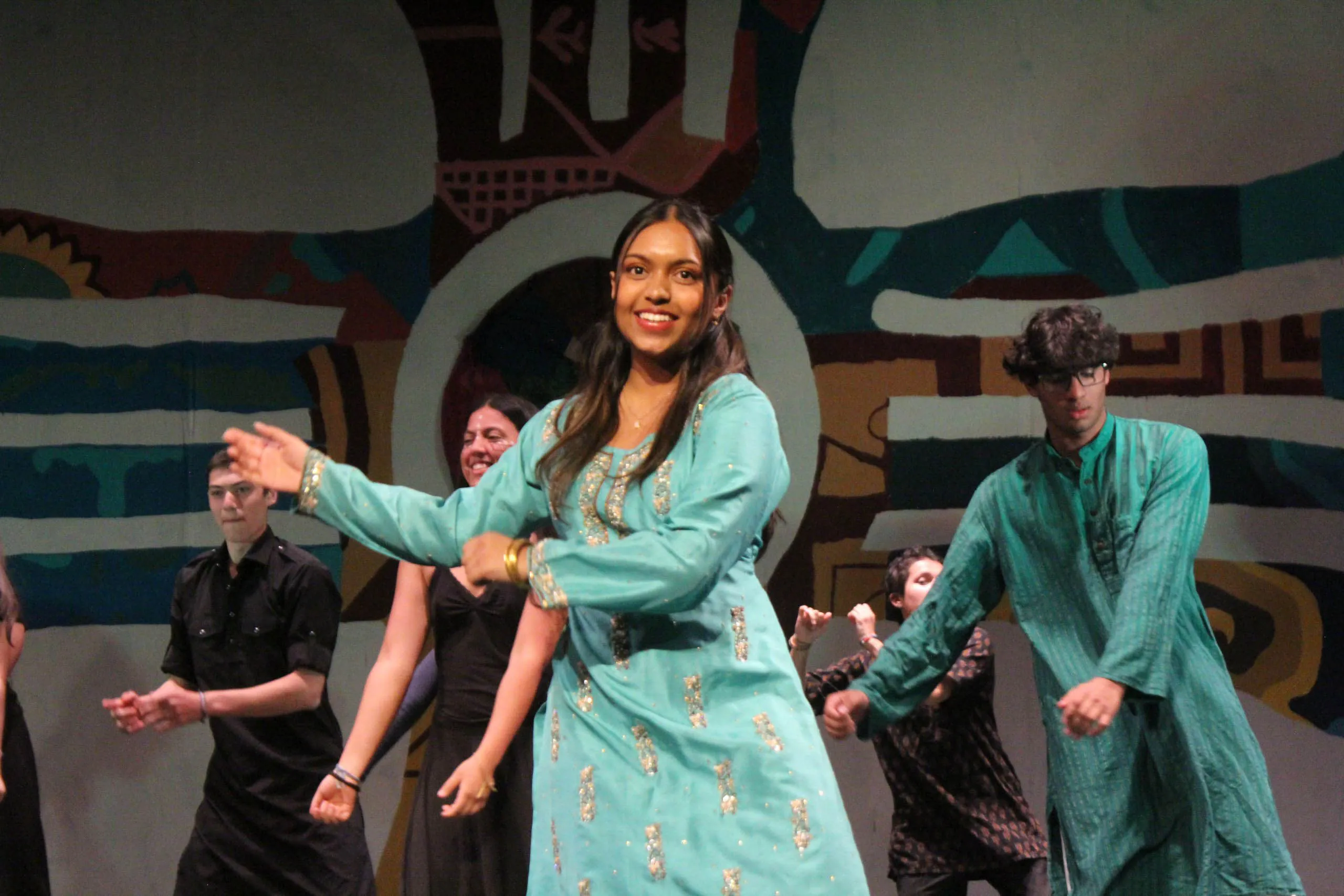 Diverse students in cultural clothes perform cultural dances on stage for an arts & culture program show.