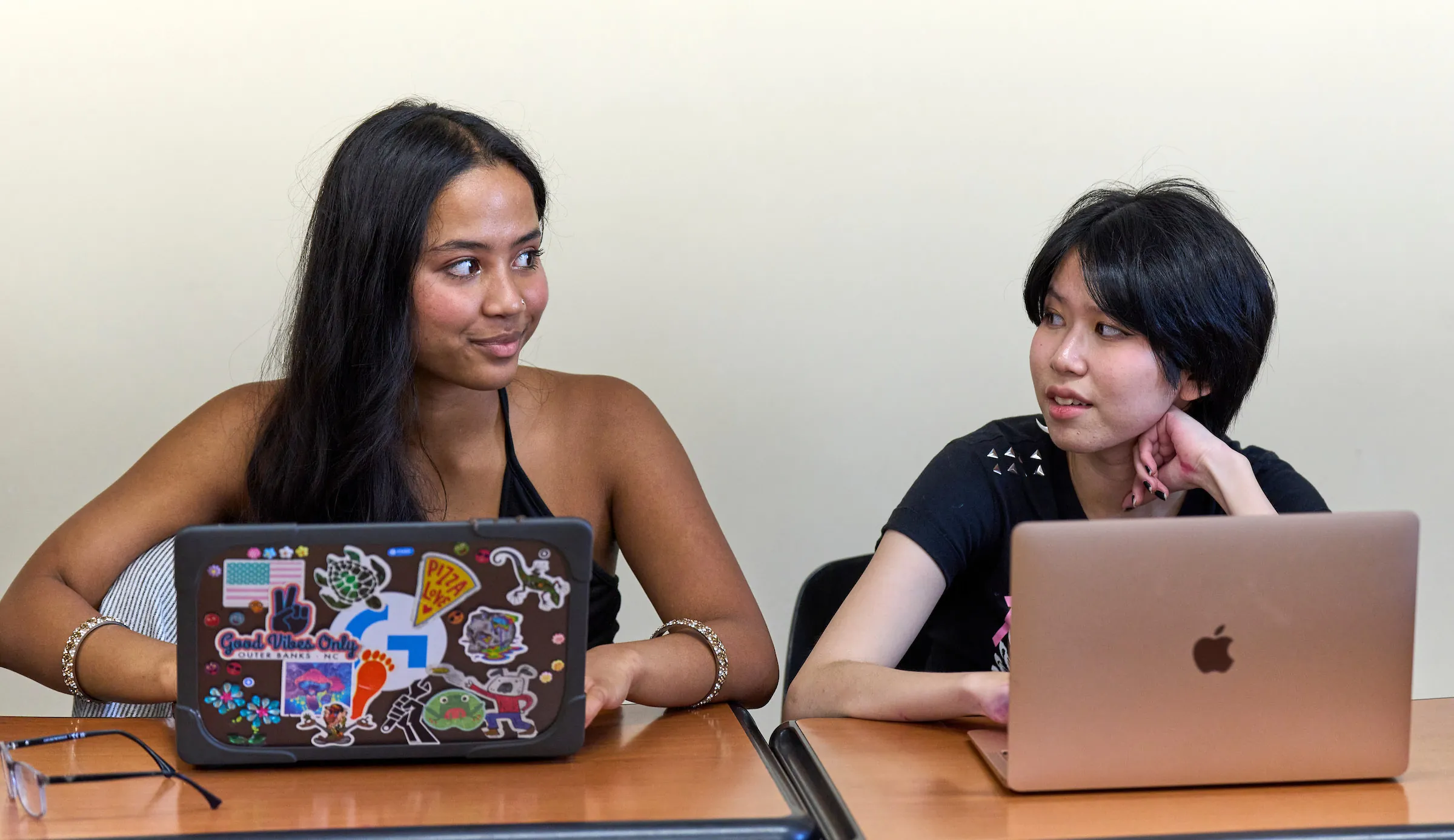 Two students in classroom on their laptops looking at each other.