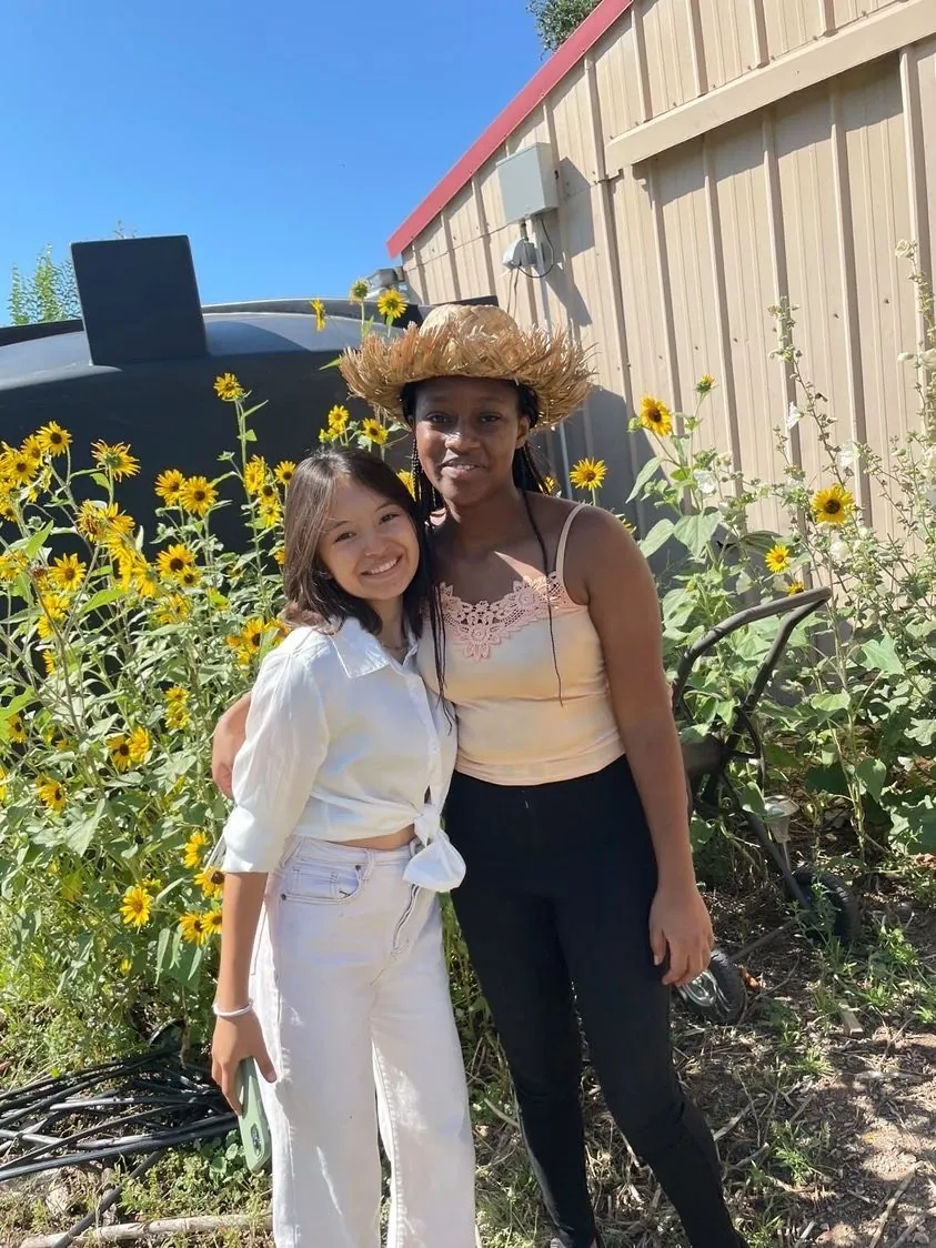Two diverse students share a moment in UWC-USA’s sunflower garden at the Farm, reflecting global friendship and commitment to sustainability.