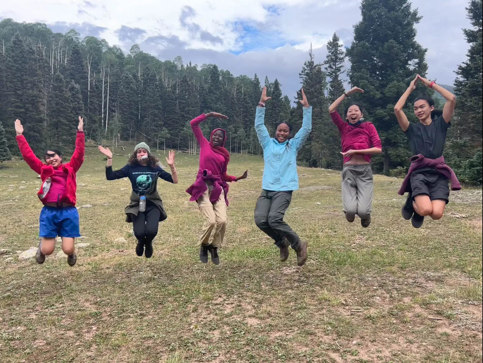 Diverse UWC-USA students celebrate global community and shared mission amid pine trees, embodying unity, joy, and outdoor learning in the New Mexico wilderness.