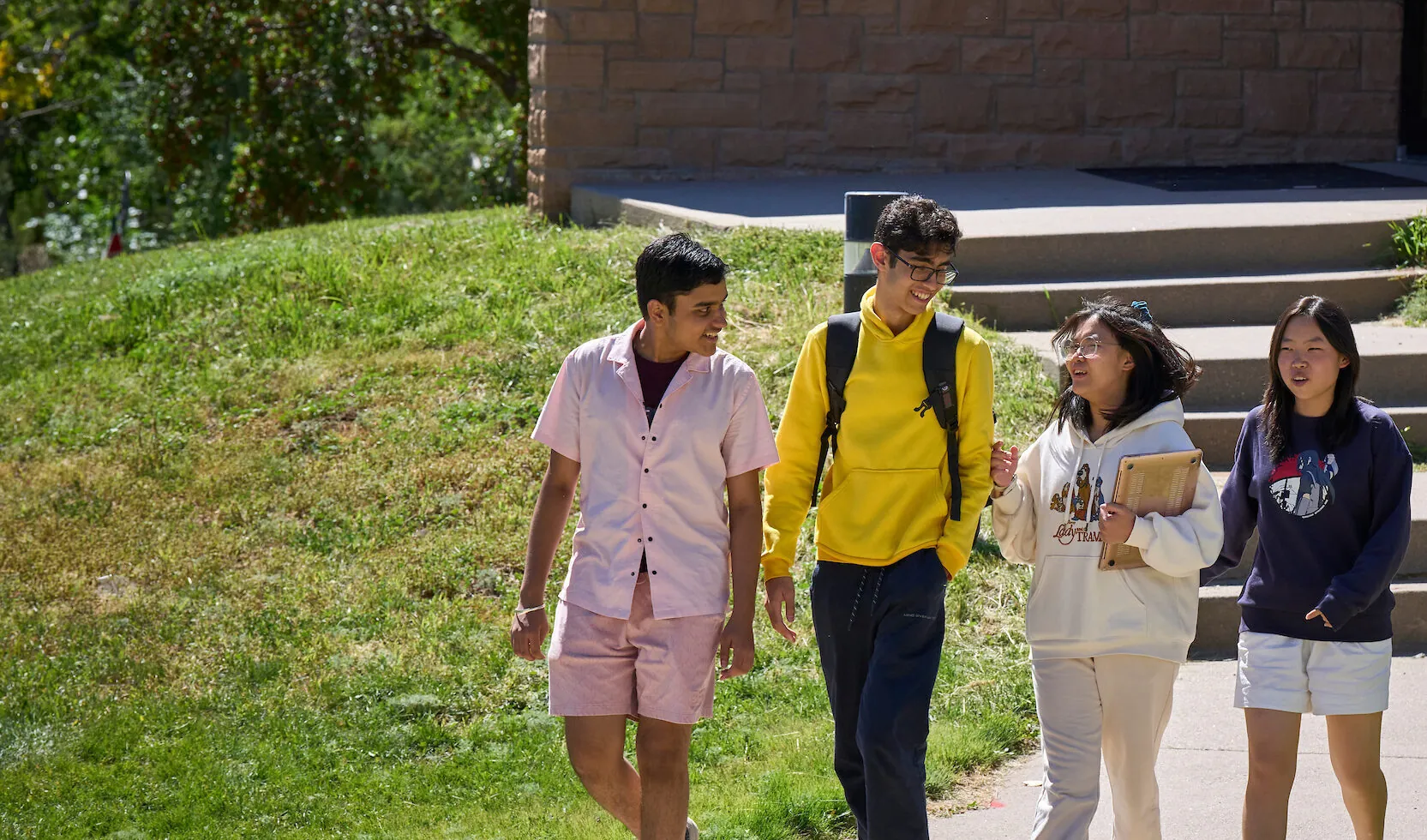 Diverse UWC-USA students share ideas outdoors, carrying books and backpacks near campus buildings, reflecting global IB academics.