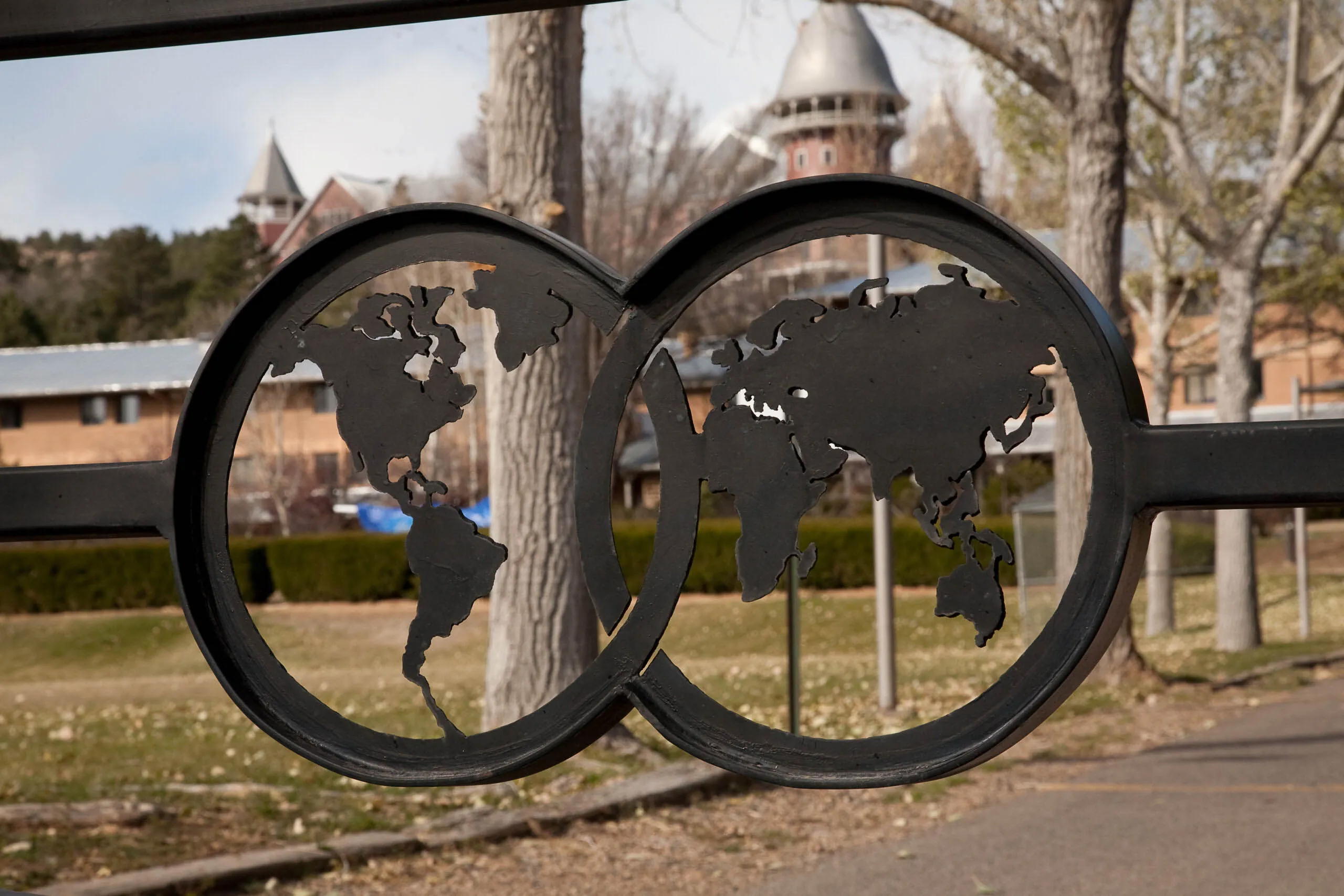 Metal gate with world map cutouts symbolizes UWC-USA’s global community, framed by campus buildings and natural landscape.