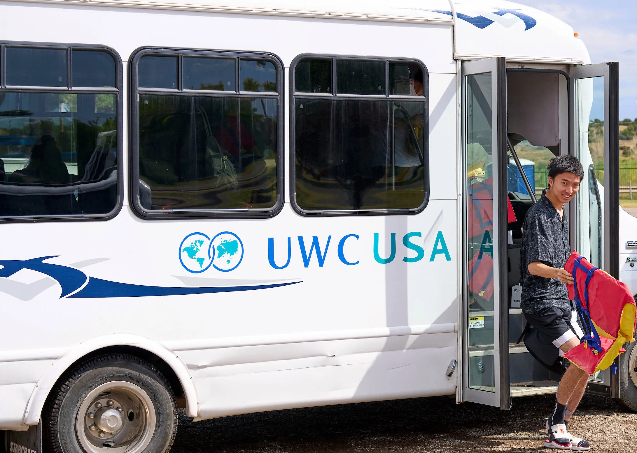 A UWC-USA student smiling as he exits the shuttle bus, embodying global community and joyful engagement.