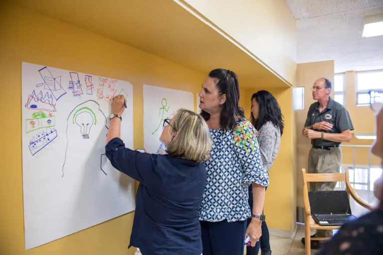 Diverse adults collaborate on creative projects during Winter IB Workshops, fostering global citizenship and community in a vibrant space.